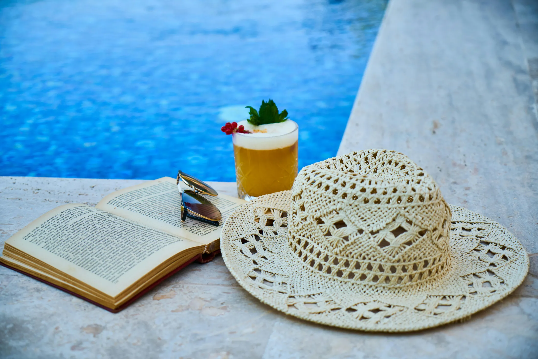 Relaxing poolside scene with a book, drink, and hat